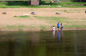 People stand in the water of a river in hot weather. Deck chairs for dancing on a background of...