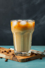 Ice coffee in a tall glass with cream poured over and coffee beans on a light stone background....