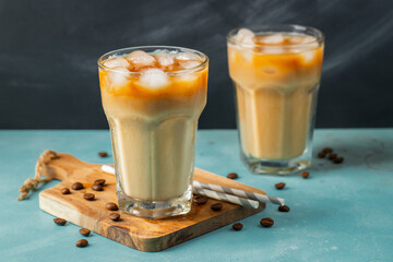 Ice coffee in a tall glass with cream poured over and coffee beans on a light stone background....