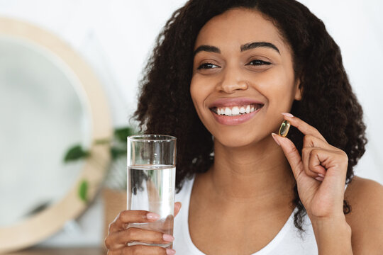 Daily Vitamins Intake. Happy Black Woman Holding Capsule Pill And Water Glass