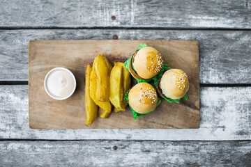 Three mini burgers with beef patty, french fries and mayonnaise on wooden board. Shabby aged table background. Unusual food serving. Fast food and unhealthy lifestyle.