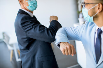 Two colleagues avoid a handshake when meeting in the office and greet with bumping elbows