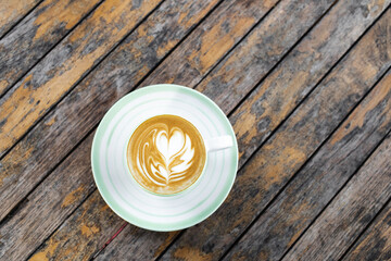 Cup of fresh creamy cappuccino with latte art on foam. Background of wooden table with shabby aged surface. Directly from above.
