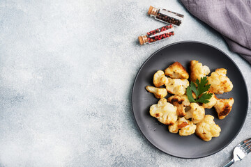 Fried cauliflower florets in batter on a black plate. Grey concrete background. Copy space.
