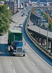 This is a big rig truck hauling a load on a busy freeway in an American city.  Daytime the road is on a slight curve in a vertical format.