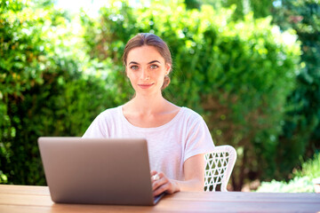 Beautiful young woman using laptop while sitting at desk outdoor