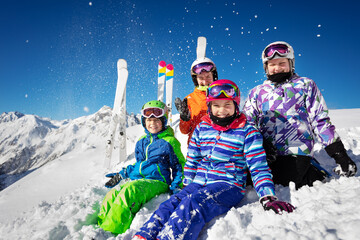 Group of ski school kids class in colorful outfit throw snow in the air sitting together over...