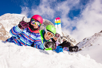 Group of happy ski kids boys and girls lay together in the snow in a row with mountain on background smiling looking at camera