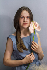 Sensual portrait of long-haired brunette girl with pink Anthurium flower on gray background