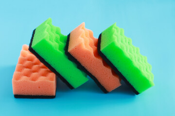 green and orange sponges for washing dishes and other surfaces on a blue background. the concept of cleaning, cleaning, disinfection.