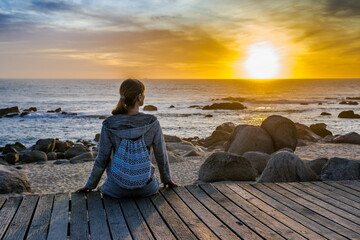 Sunset over the ocean. Portugal, the beach. Atlantic ocean in the evening. Girl tourist looking at the evening sky with orange sun. girl on the beach,
