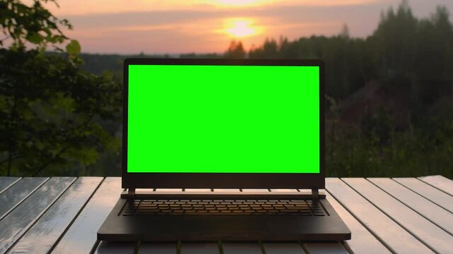 Black laptop with a green screen is on a folding table at sunset at top of mountain.