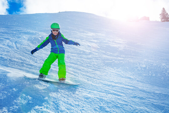 Fast action photo of a boy going downhill on snowboard view from side balancing with hands and snow powder sun backlit