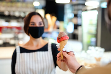 Young woman with face mask working indoors in coffee shop, serving icecream.