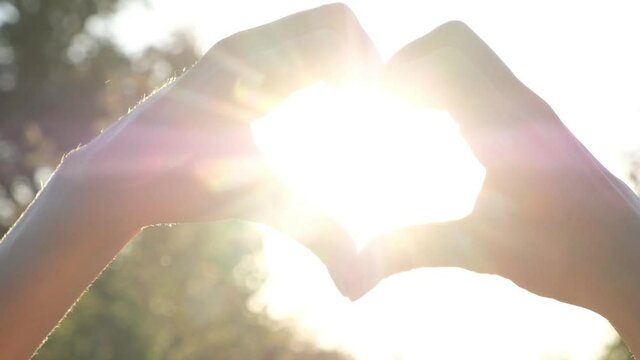 Womans Hands fold heart. The rays of the sun shine through the heart at sunset. Symbol of love, summer concept.