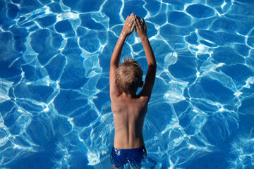 A small seven year old boy is going to jump a fish into the cool blue water of the pool