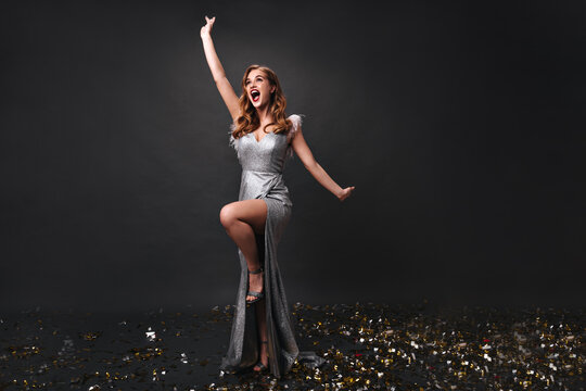 Woman in long silver dress happily posing on black background