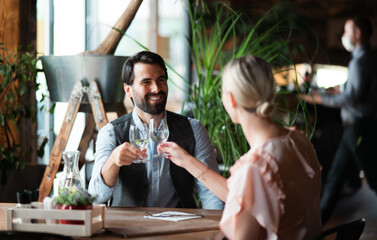 Happy couple sitting indoors in restaurant, clinking glasses.