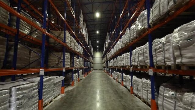 Forward shot of rows of pallets in warehouse. A path through racks of goods.