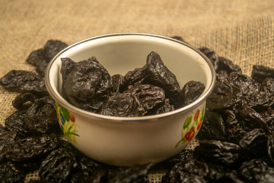 Dried prunes in a metal bowl and dried prunes scattered on a background of coarse-textured burlap. Close up.