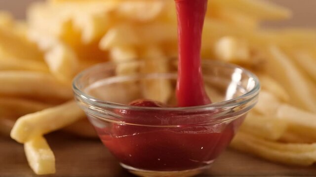 Pour tomato ketchup with french fries on background, close-up