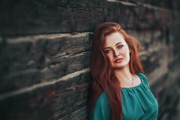 Fototapeta premium Young beautiful girl with red hair and freckles on her face, red-haired girl in a green dress on a wood background