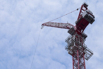 Naklejka premium Very high hoisting crane used for building skyscrapers against a cloudy blue sky