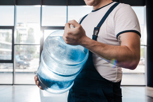 cropped view of delivery man holding heavy gallon with water