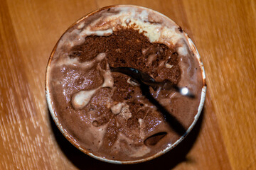 A close-up high angle view of a small bucket of melting chocolate ice cream with a spoon 