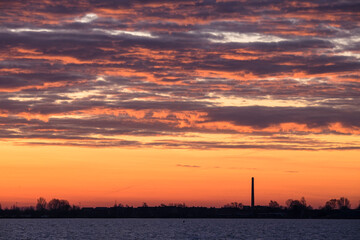 View in winter with beautiful rising sun and clouds above the Lake Tjeukemeer with chimney of a factory in the province of Friesland in the Netherlands