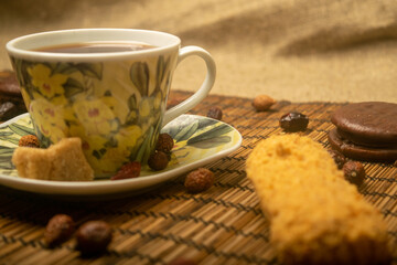 A Cup of tea, dried rosehip fruit, pieces of brown cane sugar, and cookies on a reed Mat. Close up.