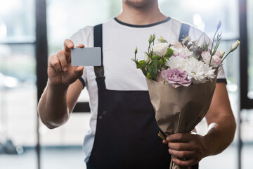 cropped view of delivery man holding bouquet with flowers and blank card