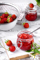 Strawberry jam in glass jar on the white wooden table. Berries around