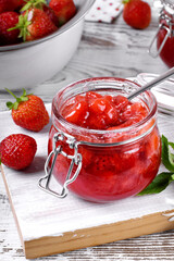 Strawberry jam in glass jar on the white wooden table. Berries around