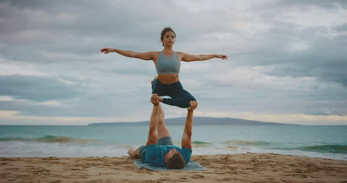 Attractive young couple practicing acro yoga on the beach, healthy wellness fitness lifestyle
