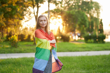 Smiling woman holding rainbow flag on shoulders.