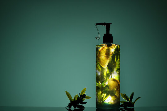 Face cleanser bottle with gel with lemon and leaves and dosator on green background. Organic beauty treatment concept. Face Care.