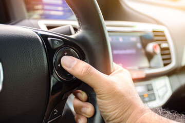 Driver pressing volume button of car radio on steering wheel of a car