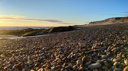 Sea, beach boulders, pebble shore and waves at sunset. Sea waves breaking on rocks. Sunny beach with sand dunes and blue sky in Esposende, Portugal.