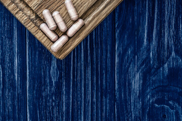 Fototapeta na wymiar Multivitamin pills on a wooden board, on an empty wooden classic blue countertop, top view