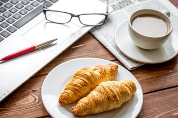 Business lunch with croissant and laptop on wooden desk