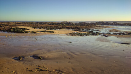 Sea, beach boulders, pebble shore and waves at sunset. Sea waves breaking on rocks. Sunny beach with sand dunes and blue sky in Esposende, Portugal.