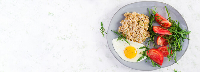 Breakfast oatmeal porridge with fried egg, tomatoes, arugula. Healthy food. Top view, overhead, banner
