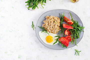 Breakfast oatmeal porridge with fried egg, tomatoes, arugula. Healthy food. Top view, overhead,  copy space