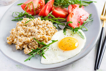 Breakfast oatmeal porridge with fried egg, tomatoes, arugula. Healthy food.