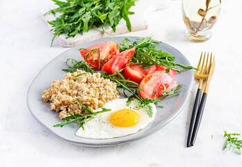 Breakfast oatmeal porridge with fried egg, tomatoes, arugula. Healthy food.
