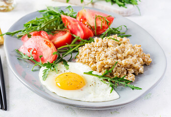 Breakfast oatmeal porridge with fried egg, tomatoes, arugula. Healthy food.