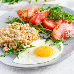 Breakfast oatmeal porridge with fried egg, tomatoes, arugula. Healthy food.