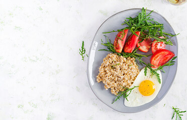 Breakfast oatmeal porridge with fried egg, tomatoes, arugula. Healthy food. Top view, overhead,  copy space