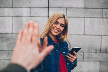 Half length portrait of attractive smiling blonde student having fun with male best best friend giving five hive at urban setting.Cropped Image of happy hipster girl looking at camera while fooling